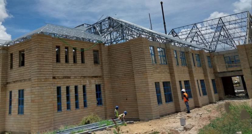 Two-storey stone commercial building under construction, with light gauge steel roof trusses being lifted into place